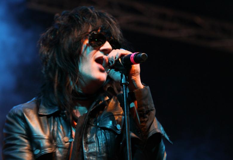 Kuvassa on Jyrki60 laulamassa nahkatakissa ja mikki kädessään. Kuva on puolivartalokuva ja tausta on tumma, vasemmalta hieman sininen. 