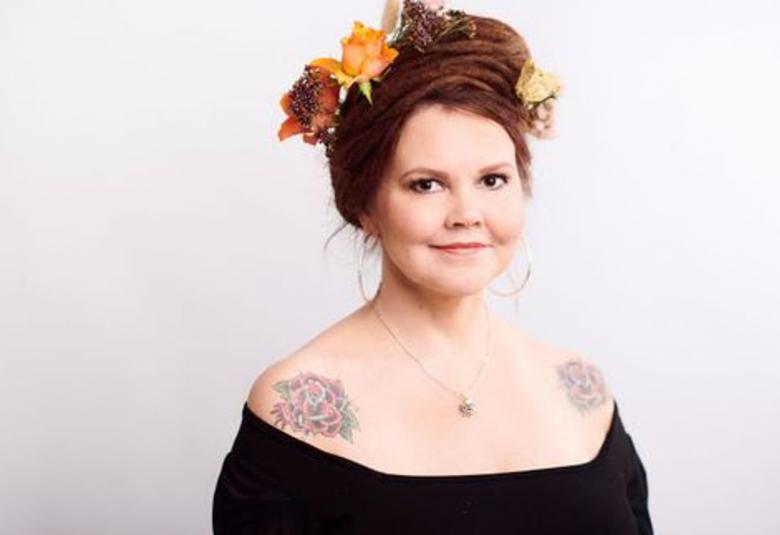 Kuvassa on Katja Kettu puolivartalokuvassa.  Hänellä on mustassa mekossaan avonainen kaula-aukko ja oikean olkaimen ruusutatuointi näkyy.  Päässään hänellä punaisissa hiuksissaan oransseja ja ruskehtavia kukkia. Tausta on vaalea.