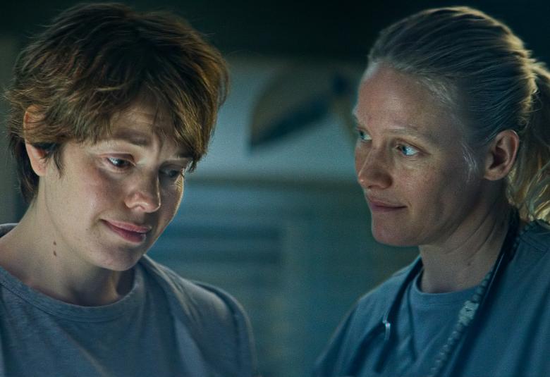 Kuvassa on vasemmalla puolivartalokuvassa Oona Airola katsomassa alaspäin ja oikealla Laura Birn katsoo Oona Airolaa. Molemmilla on vaalean siniset vaatteet.  