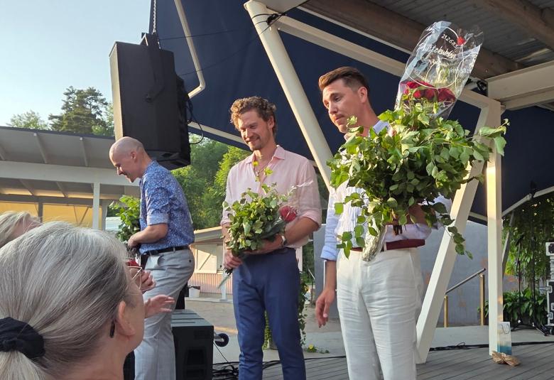 Kuvassa on vasemmalla ylempänä Ville Rusanen kumartuneen ja juttelemassa yleisön kanssa. keskellä on Kristian Lindroos vihta kädessään valkoisessa paidassa ja sinisissä farkuissa. Oikealla on Aarne Pelkonene vihta ja ruusuja kädesään vaoikessa paidassa ja farkuissa. Alhaalla näkyy yleisön päälakia.