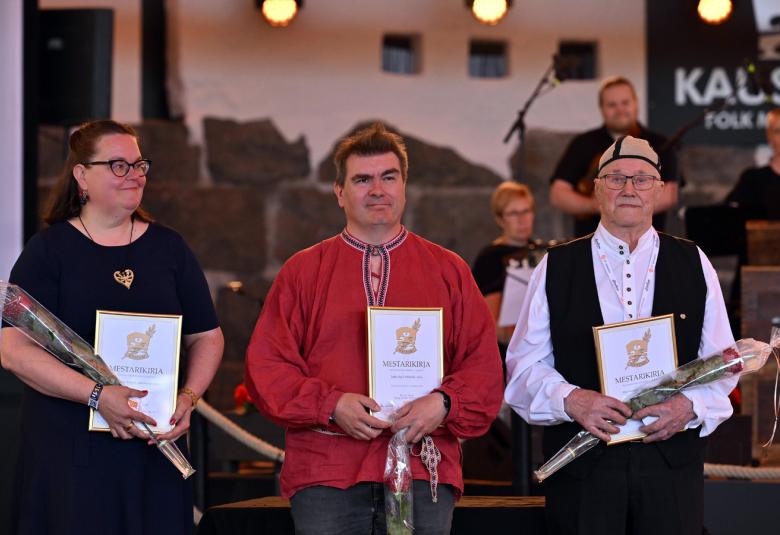 Kuvassa ovat vasemmalta Riina Sakala mustassa mekossa. Keskellä on Jaakko Kyrö punaisessa puserossa ja oikealla Alpo Suonvieri mustassa liivissä ja valkoisessa paidassa. Kaikilla on kurnniakirjat ja ruusut kädessään. 
