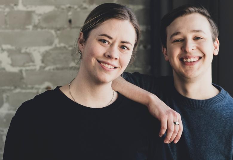 Kuvassa on vasemmalla Lotta Fors ja oikealla Jakob Norrgård. Hän pitää oikeata kättään Lotta Forsin olkapäällä. Heillä molemmilla on mustat t-paidat päällään.  Taustalla on harmaan valkeaa tiiliseinää.