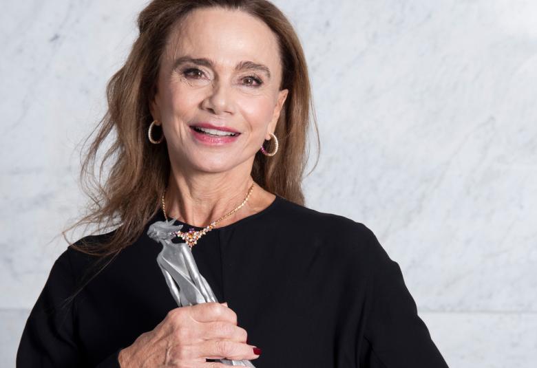 Kuvassa on Lena Olin puolivartalokuvassa mustassa mekossa ja hänellä on kädessään palkintopatsas.  