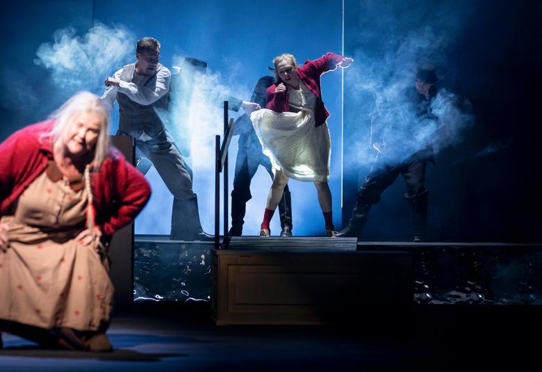 Kuvassa on vasemmalla edessä nainen kumartuneena eteenpäin ja hänellä on punainen villatakki sekä vaalean punainen mekko. Taustalla on ylempänä vasemmalla mies tumman sinisessä haalarissa ja oikealla nainen tanssimassa valkoisessa mekossa ja punaisessa villatakissa.Kuvasn sävy on sininen.