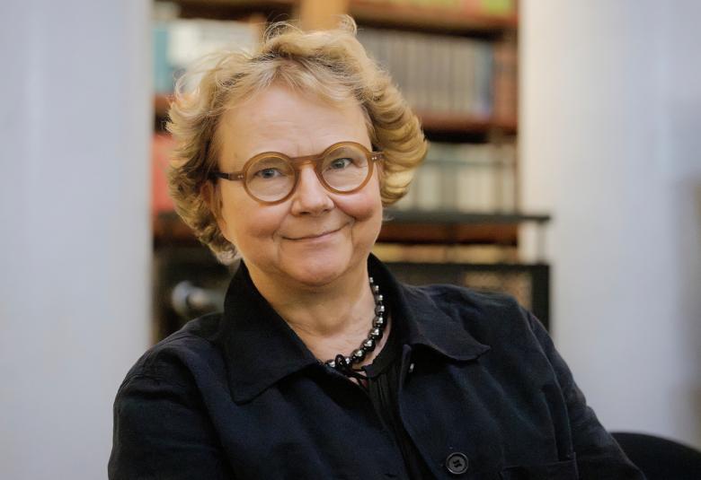 Kuvassa on Laura Kolbe puolivartalokuvassa istumassa ja hänellä on musta pusero päällään.  Taustalla on himmeästi kirjahyllyä.
