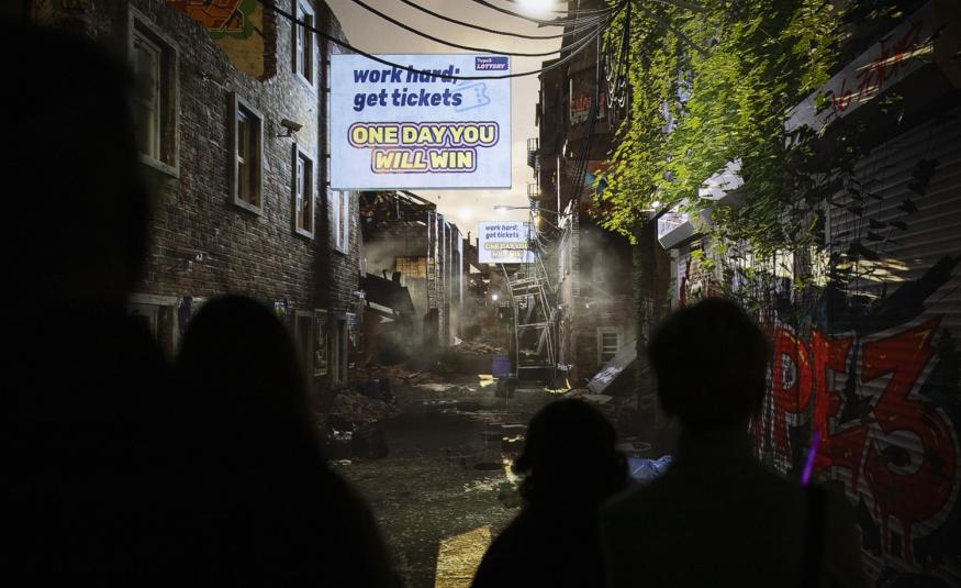 Kuvassa on tuma katunäkymä ja siinä savua ja rikkonaisia telineitä sekä kyltti, jossa lukee One day you will win.   