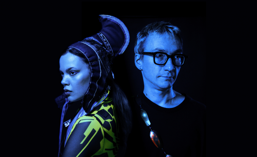 Kuvassa on puolivartalokuvassa vasemmalla Hilda Länsman sivukuvassa ja hänellä on Lapin puvun päähine ja puku. Oikealla on Tuomas Norvio mustassa t-paidassa. Kuvan sävy on tumma.