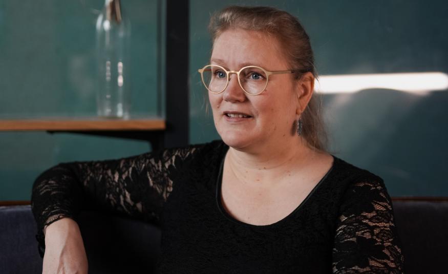 Kuvassa on Pipsa Lonka ja hän istuu puolivartalokuvassa. Hänellä on lilan värinen pusero päällään ja oikea käsi selkänojalla.