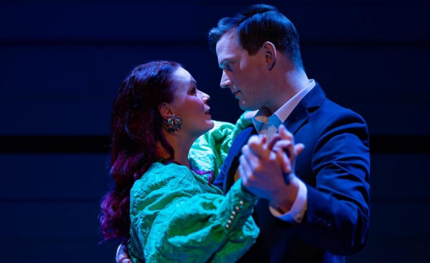 Kuvassa ovat Ella Mustajärvi vaalean vihreässä puhvihihaisessa mekossa ja Juho Markkanen tumman sinisessä takissa puolivartalokuvassa. He ovat vastakkain tanssiasennossa. Tausta on tumma.