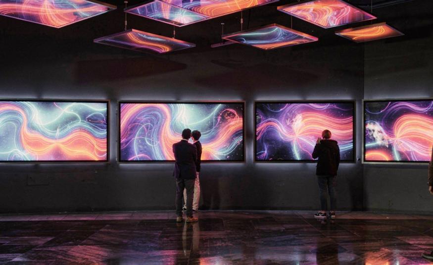 Kuvassa on keskellä ruuturivissä värikkäitä kiemurtelevia viivoja ja pintoja.  Tila on tumma ja kuvat heijastuvat kattoon ja lattiaan. Kuvia katselee pariskunta ja yksittäinen katselija.