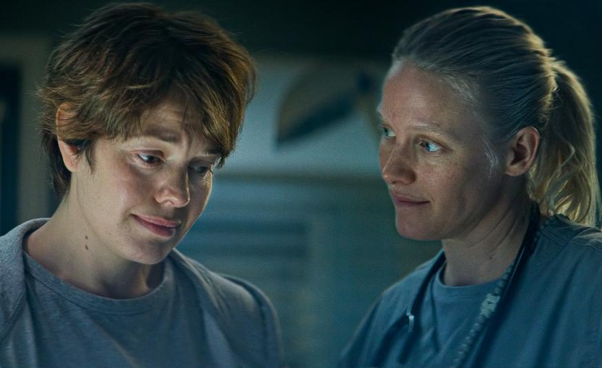 Kuvassa ovat vasemmalla puolivartalokuvassa Oona Airola ja oikealla Laura Birn himmeässä valossa. Molemmat katsovat alaspäin.