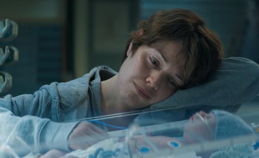 Kuvassa on Oona Airola, joka katselee keskoskaapissa nukkuvaa vauvaa. Hänellä on vaalean sininen pusero päällään. 