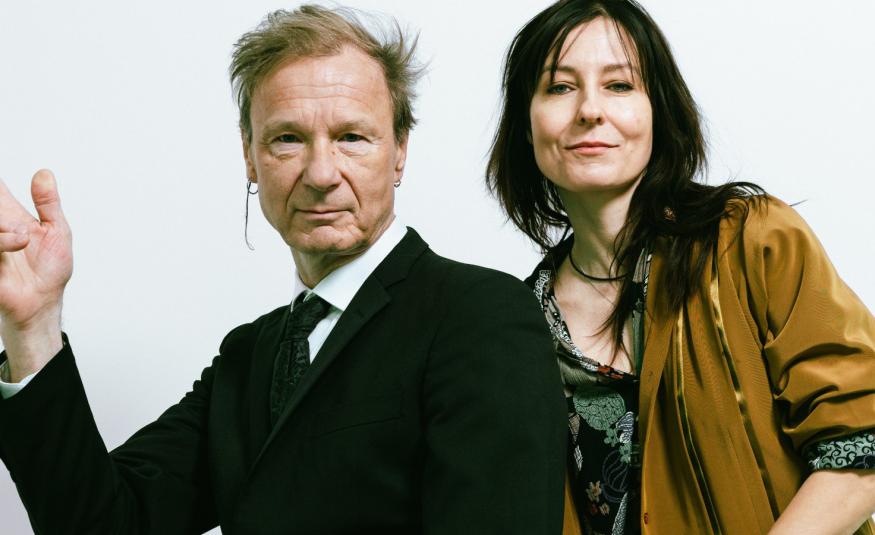 Kuvassa on vasemmalla Ismo Alanko puolivartalokuvassa mustassa takissa. Hänellä on oikea käsi nostettuna sivulle. Oikealla on Mariska ruskeassa villa takissa ja harmaassa puserossa.