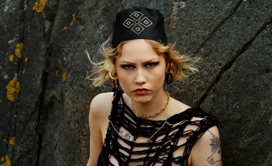 Kuvassa on Vilma Jää puolivartalokuvassa. Hänellä musta, hihaton löyhä verkkopaita päällään ja musta päähine päässään. Taustalla on tummaa kalliota.