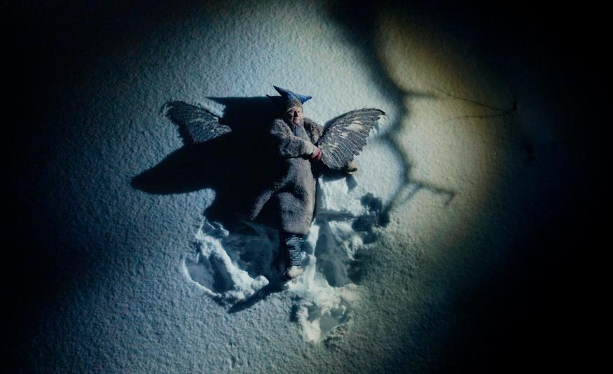 Kuvassa on mies makaamassa hangellaja hänellä on vaakasuikkahattu päässää sekä peitto päällään. Hänen vieressään näkyy tummia siipiä. Kuvaan tulee keskelle valoa ja reunat ovat tummat.