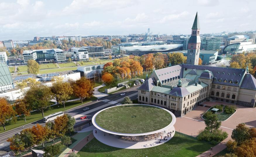 Kuvassa on ilmakuva, jossa on keskellä Kansallismuseon päärakennus ja sen takana pyöreä ruohikkokattoinen, reunasta vaalea rakennus.  Näiden vieressä menee Mannerheimintie ja sen reunassa oransseja, syksyvärisiä puita. Taustalla näkyy kaupunkia.