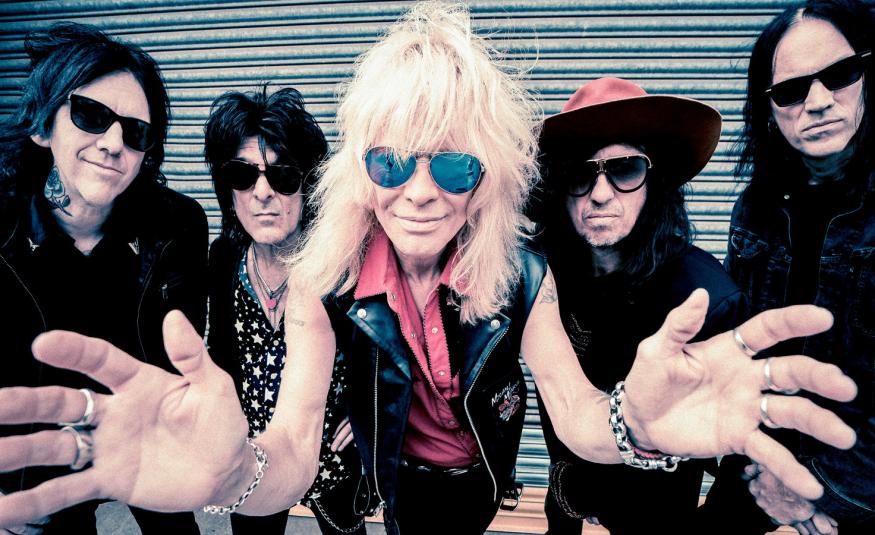 Kuvassa on keskellä Michael Monrow kädet ojennettuina eteenpäin. Hänellä on vaaleat hiukset. Taustalla on molemmin puolin kaksi bändin jäsentä ja heillä on mustat vaatteet. Kaikilla on aurinkolasit.