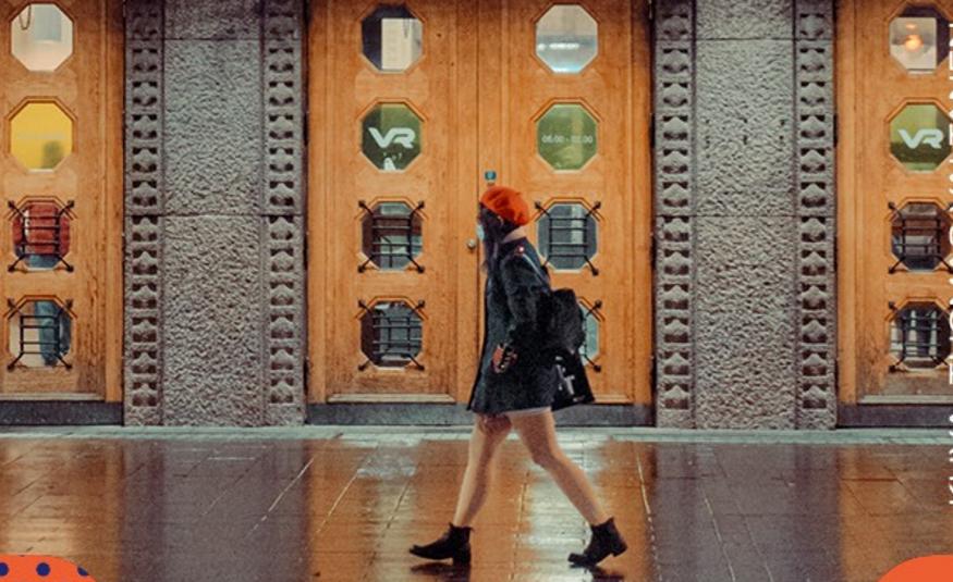 Kuvassa on Helsingin rautatieaseman pääovia, jotka ovat ruskeaa puuta ja niissä on kahdeksan pyöreää lasia. välissä on harmaata graniittia ja niissä koristeelliset reunukset. Keskellä kävelee nuori nainen mustassa takissa ja punaisessa baskerissa.