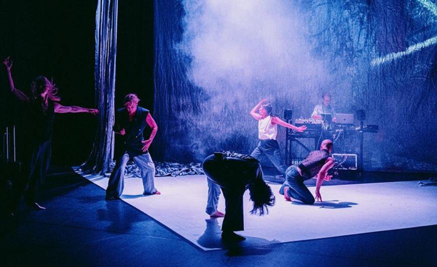 Kuvassa on sinisellä valolla valaistulla näyttämöllä neljä tanssijaa erilaisissa asennoissa. Heillä  on farkkuhouut ja eerilaisia paitoja. Keskellä on vaaleaa savua.