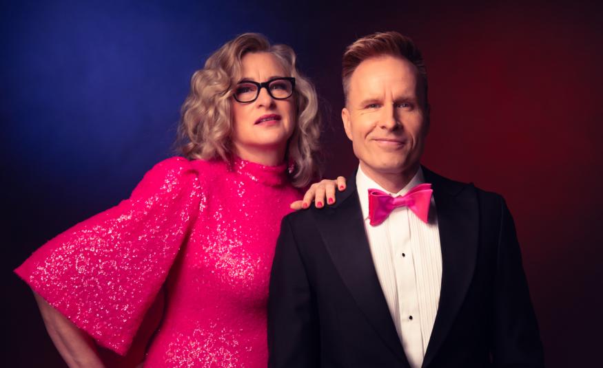 Kuvassa on vasemmalla Katja Ståhl pinkissä, glittermekossa, jossa on leveä hihat. Hän pitää vasenta kättään Mikko Kekäläisen olkapäällä, jolla on musta takki, valkoinen paita ja pinkki rusetti. He ovat puolivartalokuvassa. Tausta on tummansininen.