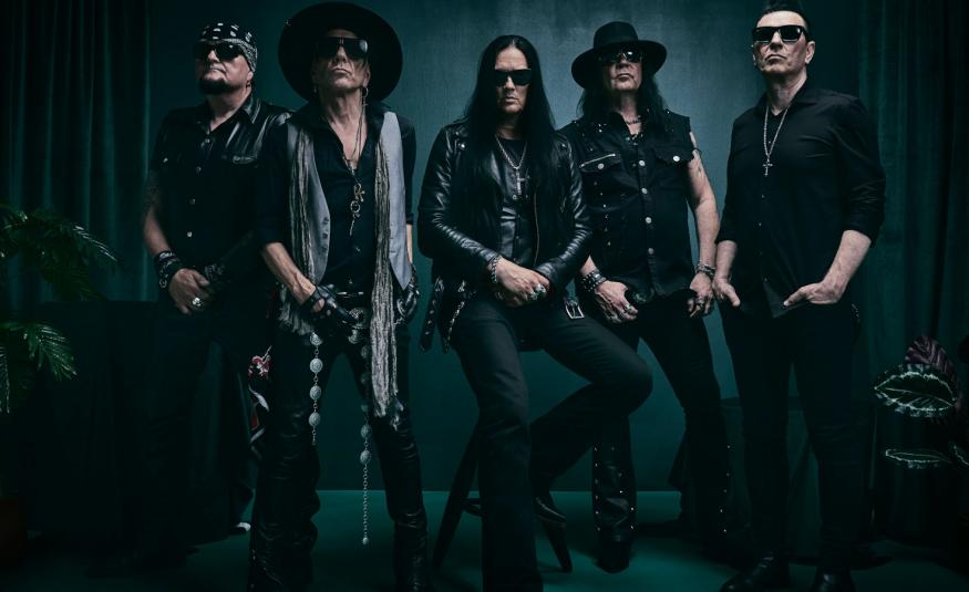 Kuvassa on viisi yhtyeen jäsentä seisomassa ja heillä on mustat vaatteet päällään. Kuvan sävy on tumma.