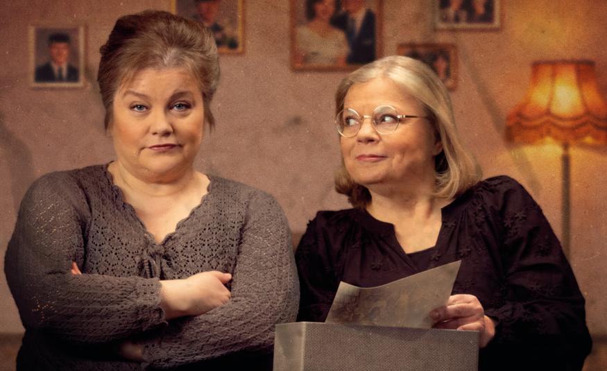 Kuvassa on vasemmalla nainen ruskeassa villapuserossa kädet puuskassa. Oikealla on nainen mustassa puserossa ja hän katsoo vasemmalla olevaa. Taustalla on huonetta.