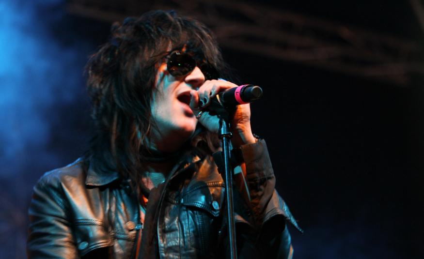 Kuvassa on Jyrki60 laulamassa nahkatakissa ja mikki kädessään. Kuva on puolivartalokuva ja tausta on tumma, vasemmalta hieman sininen. 