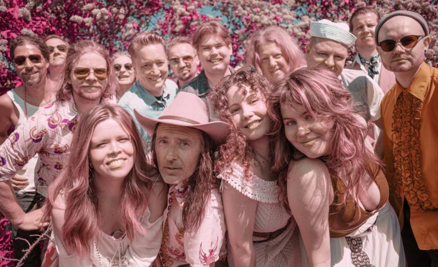 Kuvassa on puolivartalokuvassa runsaasti nuoria esiintyjiä tiiviisti vierekkäin ryhmänä koko kuva-alalla. Kuvan sävy on vaalean punainen.