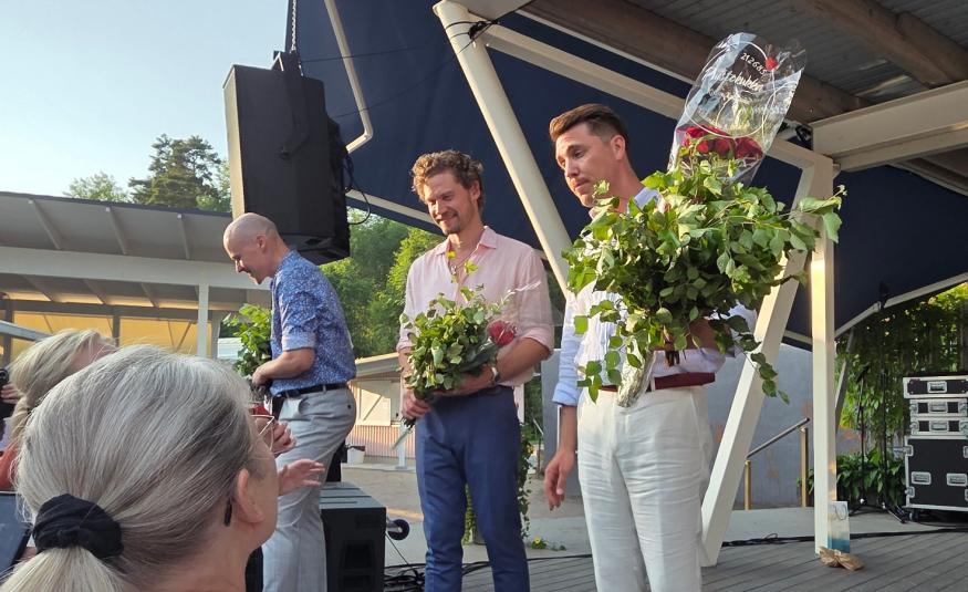 Kuvassa on vasemmalla ylempänä Ville Rusanen kumartuneen ja juttelemassa yleisön kanssa. keskellä on Kristian Lindroos vihta kädessään valkoisessa paidassa ja sinisissä farkuissa. Oikealla on Aarne Pelkonene vihta ja ruusuja kädesään vaoikessa paidassa ja farkuissa. Alhaalla näkyy yleisön päälakia.