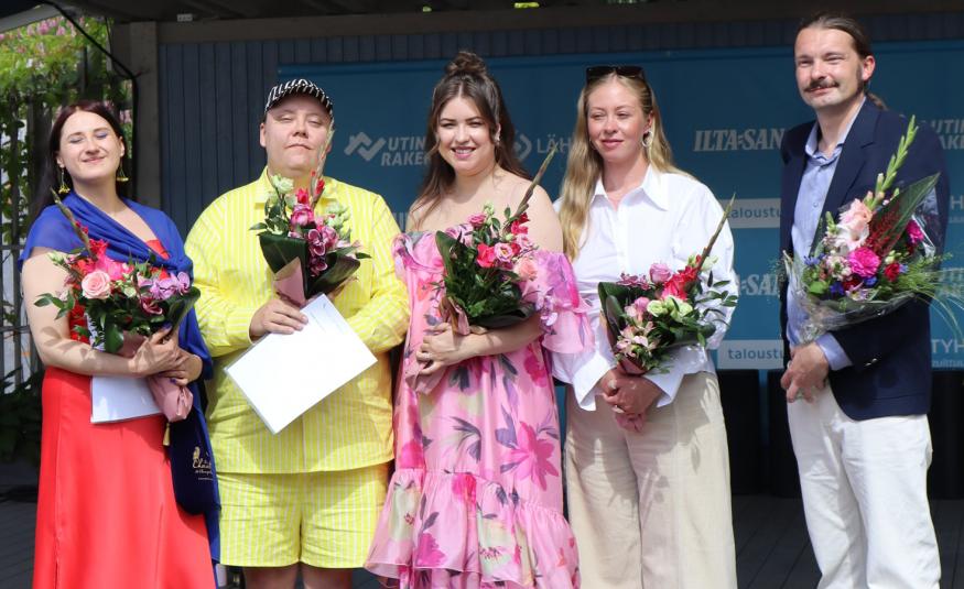 Kuvassa ovat vasemmalta Isa Suoja Rinne punaisessa mekossa, Jone Mutka keltaisessa puserossa ja shortseissa, Aino-Maija Laaksonen vaalean punaisessa kukkamekossa, Iines Niemelä vaaleassa housupuvussa ja Ilkka Aho mustassa takissa ja valkoisessa puserossa.