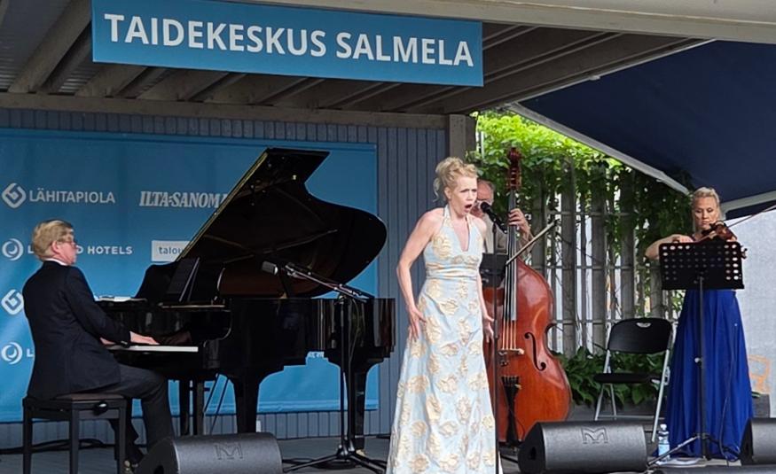 Kuvasswa on Kuvassa on vasemmalla Janne Hovi soittamassa flyygeliä ja keskellä Helena Juntunen vaaleassa, pitkässä puvussa laulamassa. Takana soittaa kontrabassoa Hannu Rantanen takana ja oikealla Maija Linkola viulua pitkässä, sinisessä puvussa. Päällä lukee Taidekeskus Salmela.