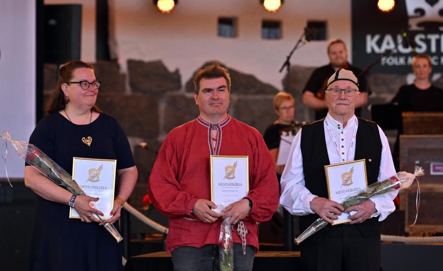 Kuvassa ovat vasemmalta Riina Sakala mustassa mekossa. Keskellä on Jaakko Kyrö punaisessa puserossa ja oikealla Alpo Suonvieri mustassa liivissä ja valkoisessa paidassa. Kaikilla on kurnniakirjat ja ruusut kädessään. 