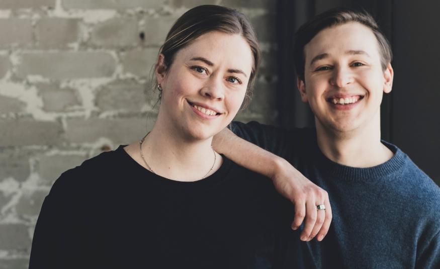 Kuvassa on vasemmalla Lotta Fors ja oikealla Jakob Norrgård. Hän pitää oikeata kättään Lotta Forsin olkapäällä. Heillä molemmilla on mustat t-paidat päällään.  Taustalla on harmaan valkeaa tiiliseinää.