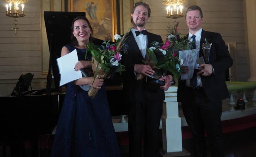 Kuvassa ovat seisomassa kukat käsissään vasemmalta Maria Turunen mustassa mekossa, Kristian Lindroos mustassa puvussa kuten myös Tni Hintsala. Taustalla on Mäntyharjun kirkon alttaritaulu ja kaksi kynttiläkruunua.