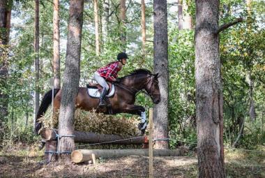 Kuvassa on Olga Temonen ratsastamassa metsässä.  Hevonen on ruskea.