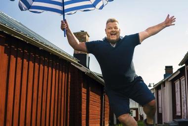 Kuvassa on Jari Sillanpää, joka hyppää sini-valkoinen päivänvarjo oikeassa kädessään. Hänellä on tumman sininen t-paita ja shortsit  päällään. Taustalla on katu, jossa on punaisia, matalia rakennuksia.