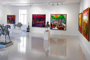 Kuvassa on Reidar Särestöniemen teoksia valkoisen salin seinillä.  Ne ovat värikkäitä. Lisäksi on lattialla harmaita veistoksia ja vasemmalla edessä on kaksi ratsastajaa hevosen selässä. Taaempana on harmaa härkäveistos. Keskellä on myös hevonen.