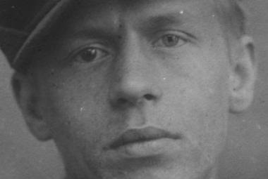 Kuvassa on Jalmari Ruokokosken kasvot musta-valkokuvassa. Hänellä on lippalakki päässään. Kuvan sävy on harmaa.