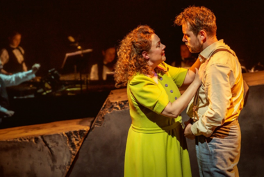 Kuvassa ovat etualalla seisomassa vasemmalla vaalean vihreässä mekossa Pihla Penttinen, joka pitää käsiään Waltteri Torikan rinnalla. Hänellä on vaalean ruskea pusero ja harmaat housut. Taustalla on himmeästi orkesteri tummalla taustalla.