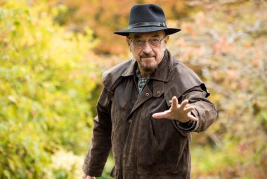 Kuvassa on Jethro Tull seisomassa ruskeassa nahkatakissa ja hattu päässään.  Hän osoittaa vasemmalla kädellään eteenpäin. Taustalla on vihreitä pensaita.