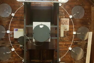 Kuvassa on iso ikkuna, josta näkyy asemahalliin ja siellä kävelee ihmisiä. Edessä näkyy pöytää ja molemmin puolin on vaalean ruskeat pylväät.