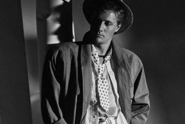 Kuvassa on nuori mies lierihatussa ja väljässä takissa ja paidassa. Kuva on musta-valkoinen.