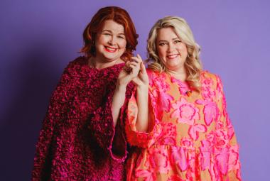 Kuvassa on vasemmalla seisomassa Ani Kellomäki viininpunaisessa mekossa  ja Tiia Koivusalo pinkissä mekossa. Tausta on lila.