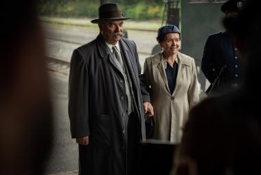 Kuvassa ovat vasemmalla Pertti Sveholm harmaassa takissa. Hänen vieressään oikealla on ruskehtava takki päällään. Mustaa on kuvan molemmissa reunoissa.