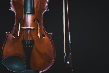 Kuvassa on mustalla pohjalla tumman ruskea viulu pystyssä. 