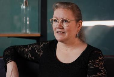 Kuvassa on Pipsa Lonka ja hän istuu puolivartalokuvassa. Hänellä on lilan värinen pusero päällään ja oikea käsi selkänojalla.