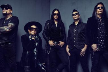 Kuvassa on tumman harmaalla pohjalla The 69 eyes -bändin viisi miestä mustissa vaatteissa, joista neljä seisoo ja yksi istuu. 