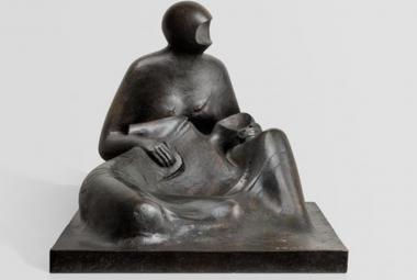 Kuvassa on veistos, joka on musta ja siinä on kasvot koverrettu naishahmo istumassa ja pitelemässä toista ihmishahmoa, joka on makuuasemmossa hänen sylissään. Kuva on musta-valkoinen.