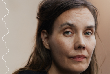 Kuvassa on keskellä lattialla makaava nainen ja häntä hoitaa toinen nainen. Molemmin puolin seisoo jonossa miehiä ja naisia ja heillä on tavalliset vaatteet. Tausta on tumma.