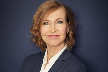 Kuvassa on Leena Niemistö ja hän on puolivartalokuvassa. Hänellä on tumman sininen jakku ja valkoinen paitapusero päällään sekä puolipitkät, kiharat punertavat hiukseton. Tausta on tumman sininen. 